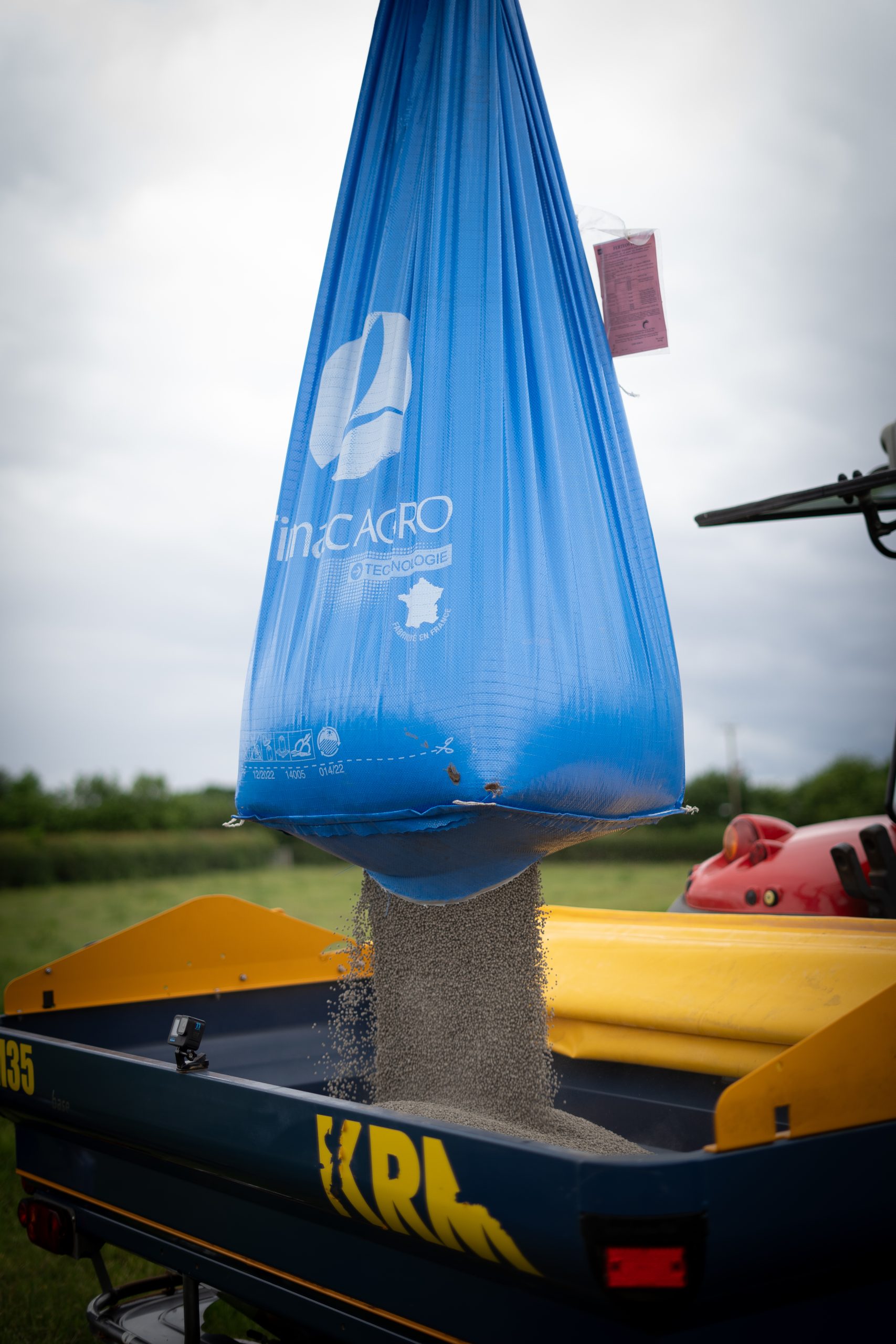 Large blue bag of TIMAC AGRO fertiliser being emptied into spreader.